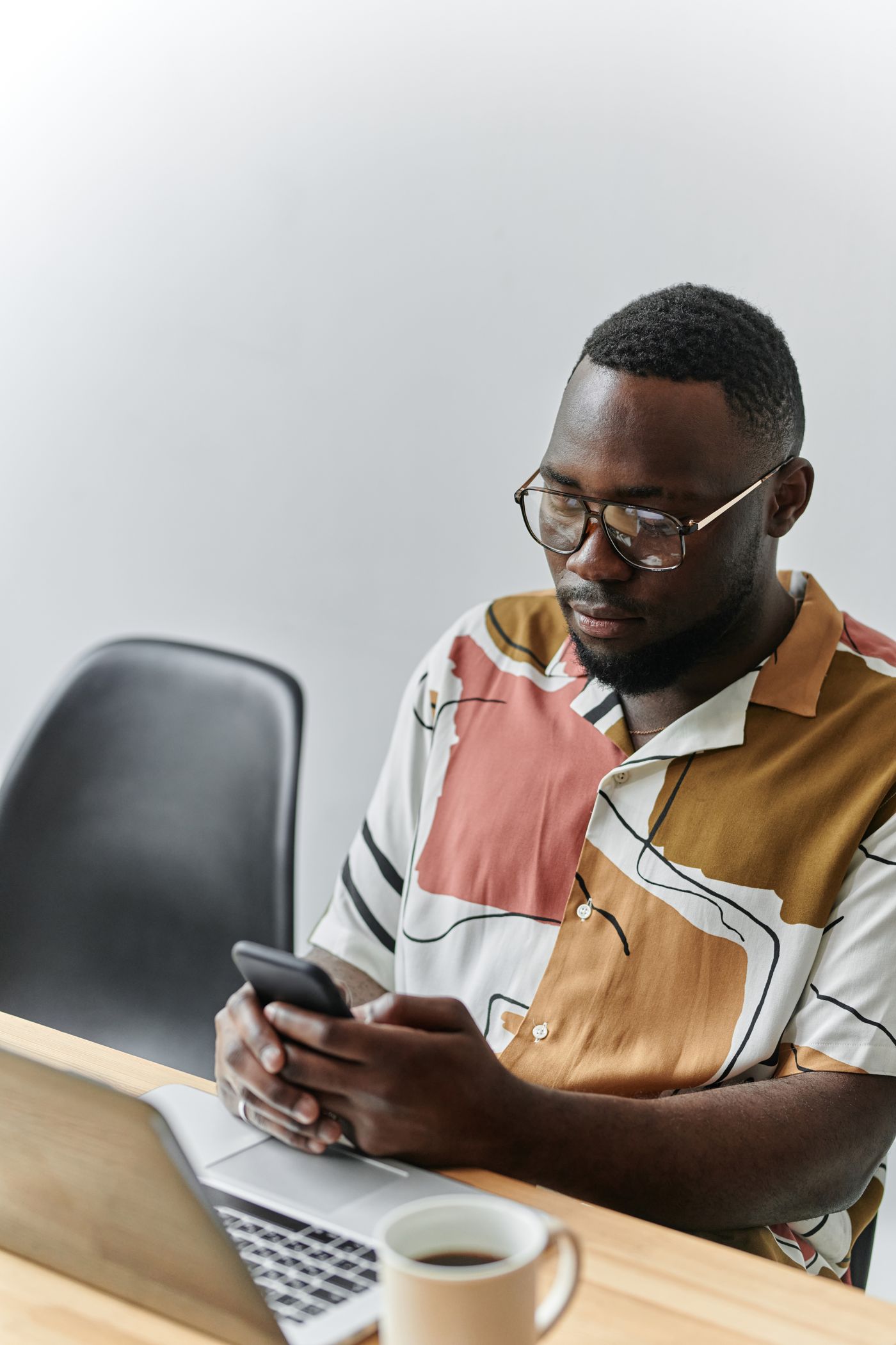 A professional using a smartphone beside a laptop at work